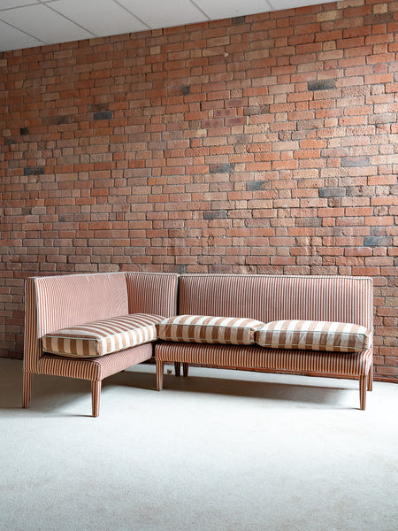 Sectional sofa with striped cushions against a brick wall.