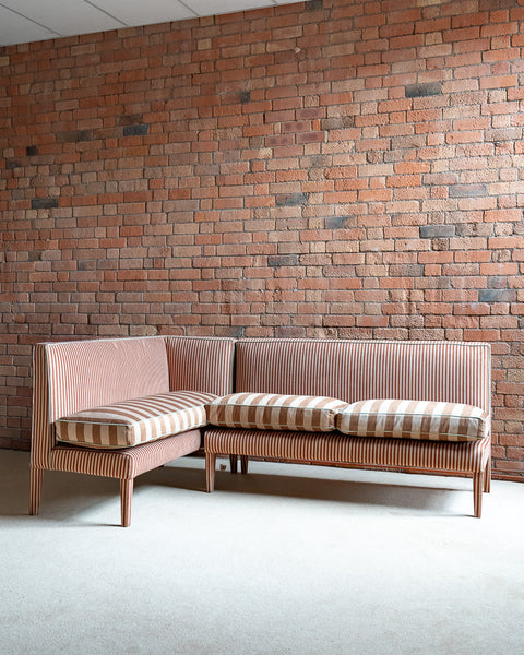 Sectional sofa with striped cushions against a brick wall.