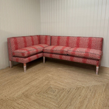 Red patterned sectional sofa in a room with wooden flooring and white walls.