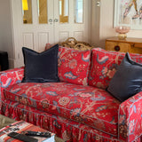 A red floral ruffled sofa slipcover with two dark navy velvet throw pillows, styled in a cozy living room setting.