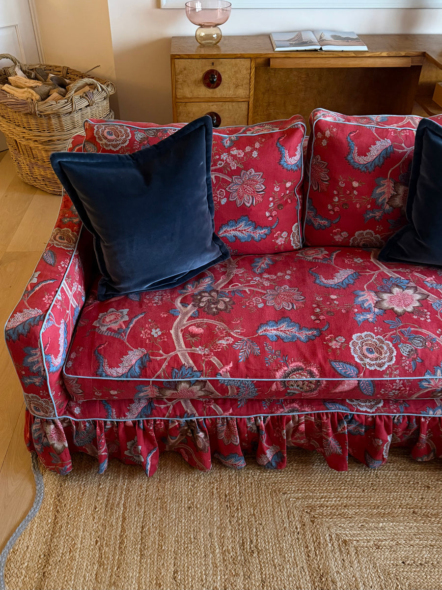 A red floral sofa top down view with a ruffled skirt and two dark navy velvet throw pillows, shown in a cozy living room setting.