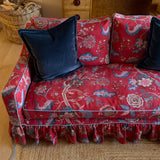 A red floral sofa top down view with a ruffled skirt and two dark navy velvet throw pillows, shown in a cozy living room setting.