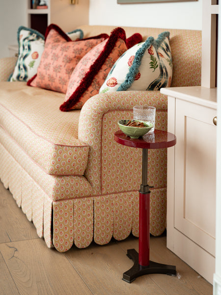 Side profile of the Symington scalloped sofa showing the rolled-arm detail and piping, set next to a small red lacquered side table.
