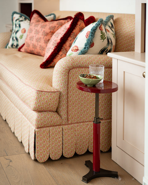 Side profile of the Symington scalloped sofa showing the rolled-arm detail and piping, set next to a small red lacquered side table.
