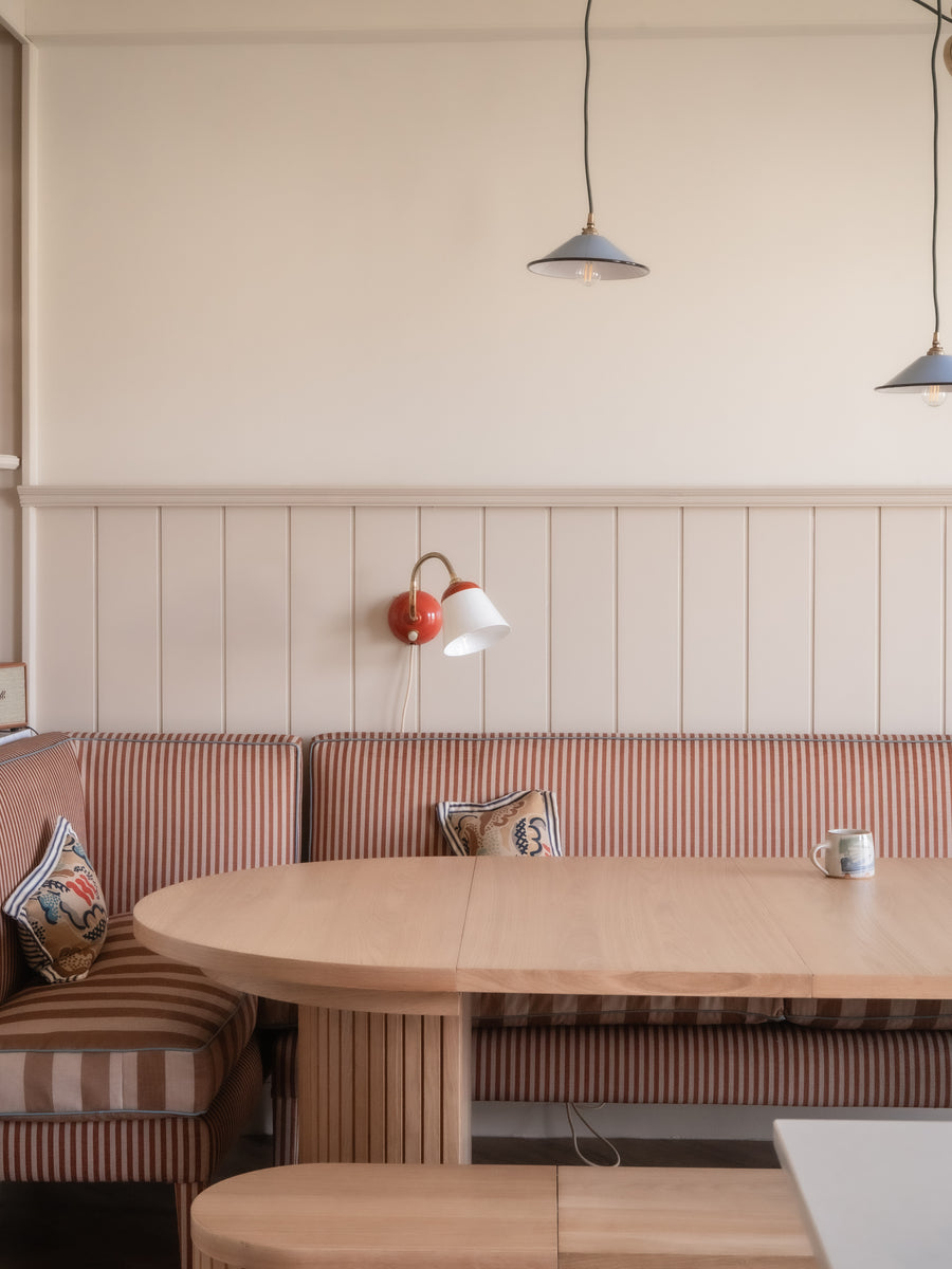 Dining area with wooden table and striped bench against a light-colored wall.