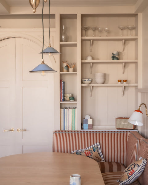 Modern interior with a wooden table, striped sofa, and shelves with decor items.
