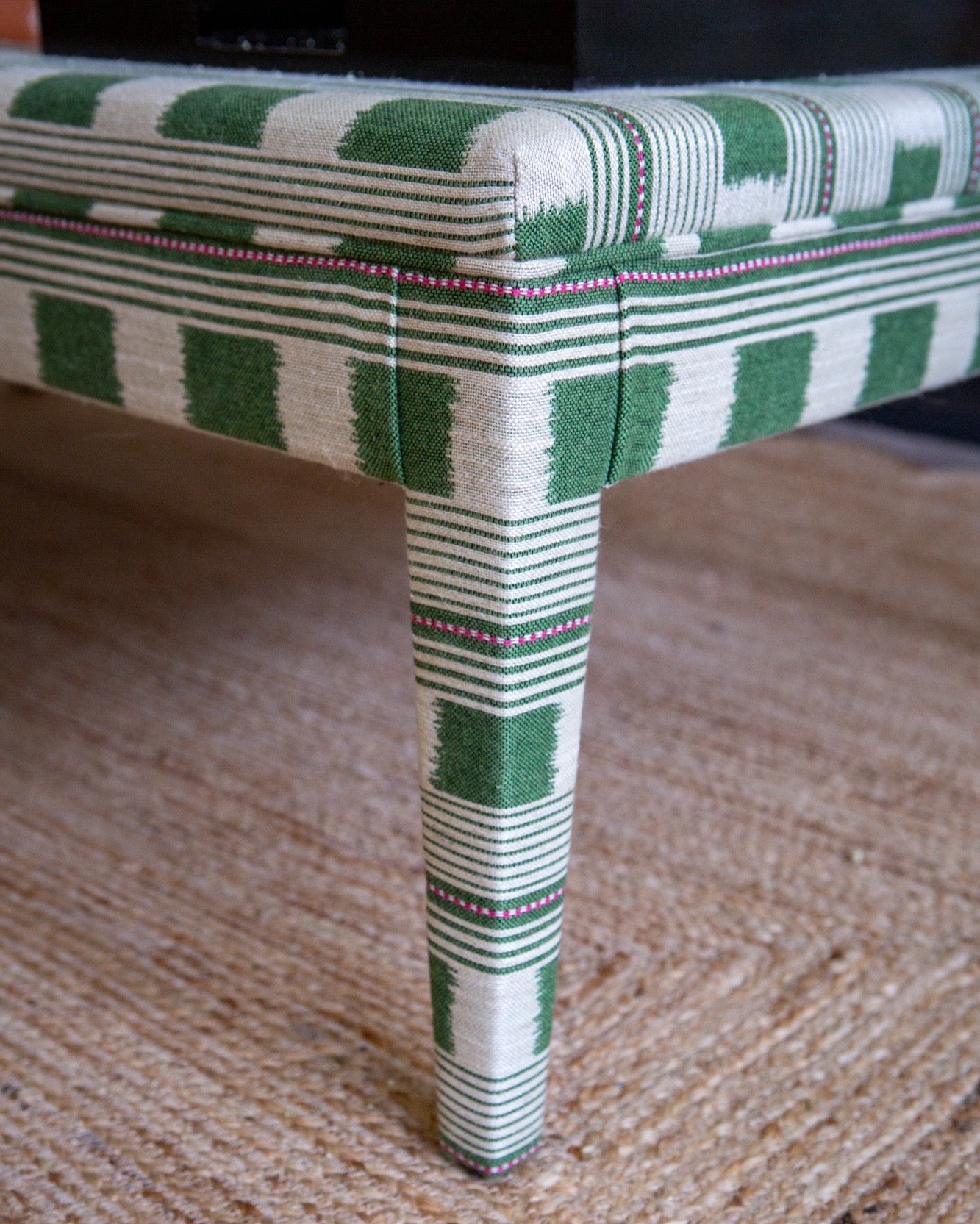 Close up view of the corner of a Honey upholstered coffee table in Green Christopher Farr Lost & Found fabric